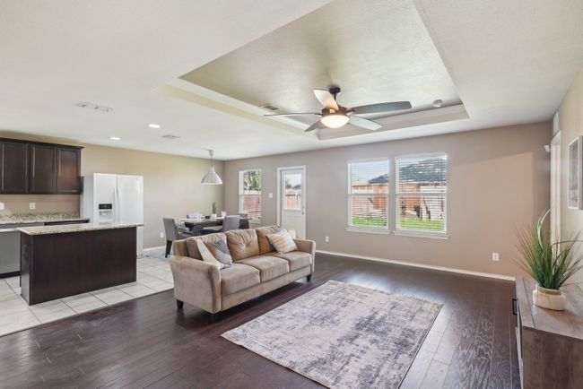Living room featuring baseboards, a raised ceiling, light wood-style floors, ceiling fan, and visible vents | Image 6
