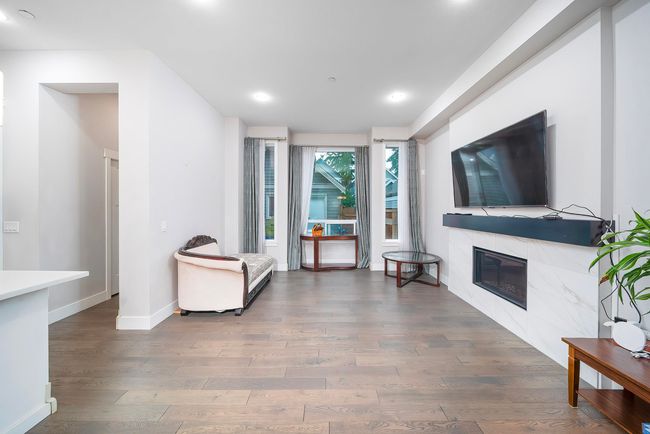 Living room featuring wood finished floors, a glass covered fireplace, baseboards, and recessed lighting | Image 8