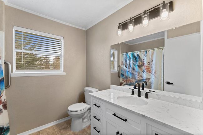 Bright bathroom featuring a modern vanity with a marble countertop, stylish black fixtures, and a large mirror. There's a shower and a window providing natural light. Neutral-toned walls and tile flooring complete the look. | Image 27