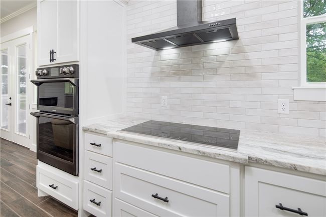 Kitchen with wall chimney exhaust hood, multiple ovens, black electric stovetop, ornamental molding, and dark wood-style flooring | Image 5