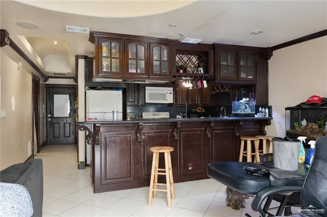 Bar with white appliances, backsplash, light tile patterned floors, ornamental molding, and dark brown cabinetry | Image 11