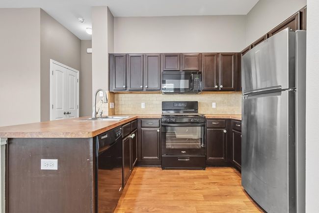 Kitchen with black appliances, a peninsula, dark wood cabinets, light countertops, and backsplash | Image 9