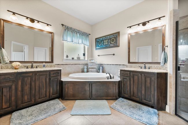 Bathroom featuring tile flooring, two vanities, a shower stall, a bath, and tile walls | Image 12