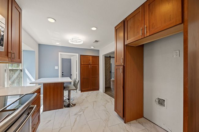 Kitchen featuring light countertops, a breakfast bar, brown cabinetry, marble finish floor, and visible vents | Image 8