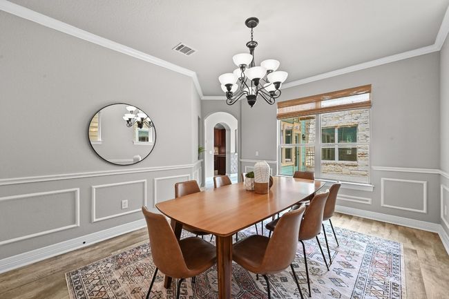 Dining area with a chandelier, arched walkways, light wood-like finished floors, crown molding, and wainscoting | Image 15