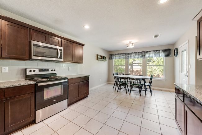 Kitchen featuring visible vents, light tile patterned floors, appliances with stainless steel finishes, dark brown cabinets, and decorative backsplash | Image 13