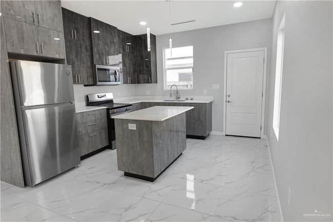 Kitchen with light countertops, stainless steel appliances, a center island, marble finish floor, and a sink | Image 6