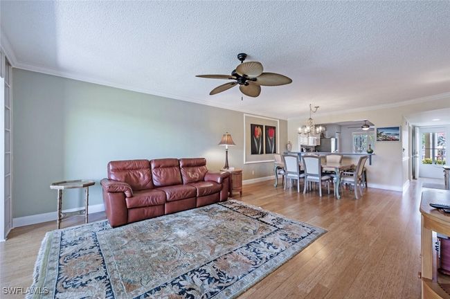 Living area with ceiling fan with notable chandelier, crown molding, a textured ceiling, and wood finished floors | Image 5