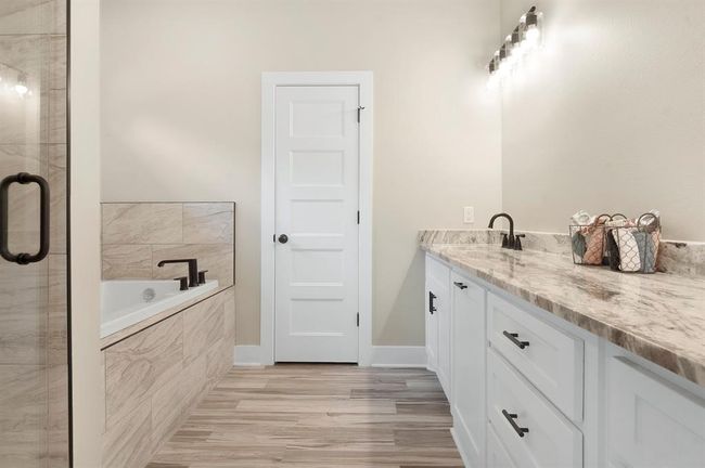 This bathroom features a modern design with a spacious vanity, marble countertops, and ample lighting. A sleek bathtub with stylish fixtures complements the neutral tile and flooring, creating a serene, elegant space. | Image 18