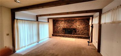 Unfurnished living room featuring a textured ceiling, beam ceiling, light tile patterned flooring, and a fireplace | Image 2