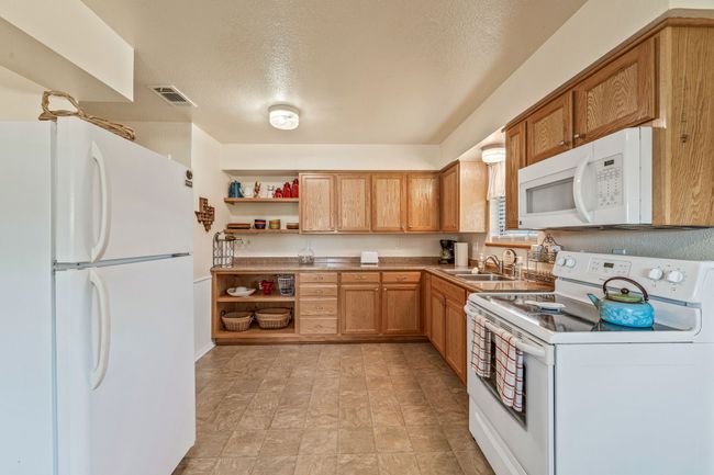 Kitchen featuring white appliances, a textured ceiling, open shelves, visible vents, and a sink | Image 12