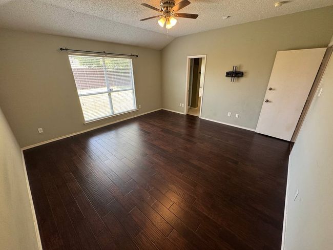 Empty room with a textured ceiling, lofted ceiling, dark wood finished floors, and ceiling fan | Image 10