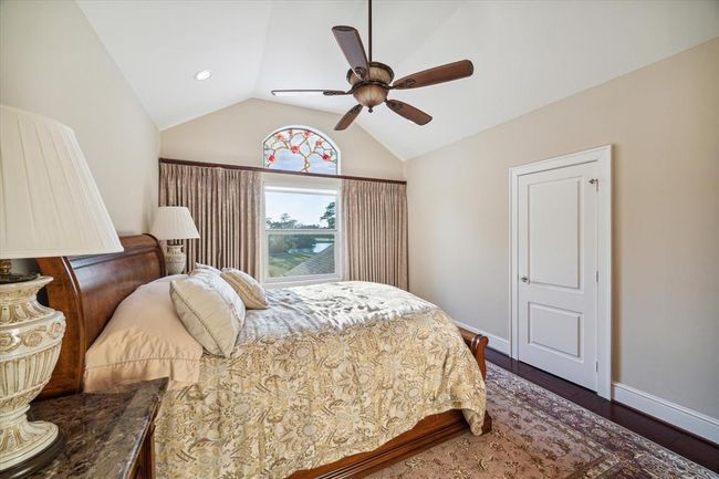 Cozy bedroom with vaulted ceiling, featuring a ceiling fan and a large window with decorative glass, creating a warm and inviting atmosphere. | Image 20