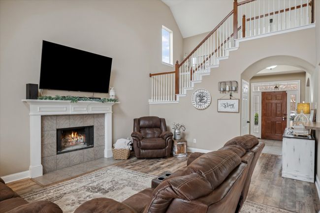 Living area featuring baseboards, arched walkways, a tiled fireplace, wood finished floors, and high vaulted ceiling | Image 6
