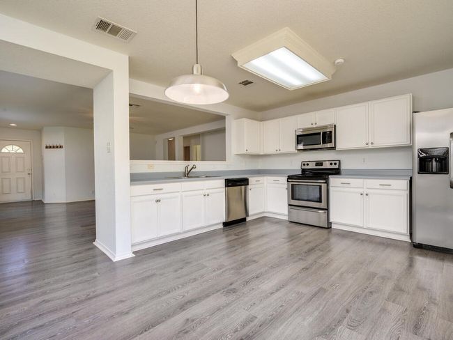 Kitchen featuring appliances with stainless steel finishes, white cabinets, luxury vinyl wood-look flooring, and light countertops. | Image 13