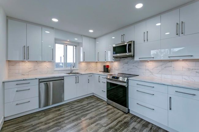 Kitchen featuring stainless steel appliances, a sink, dark wood-style flooring, white cabinetry, and light stone counters | Image 10