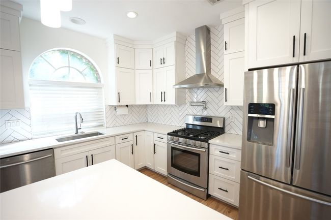 Kitchen featuring appliances with stainless steel finishes, wall chimney range hood, white cabinets, light stone counters, and tasteful backsplash | Image 5