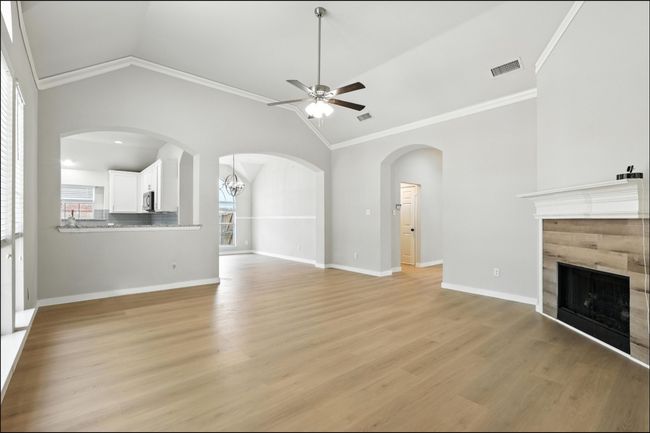 Unfurnished living room with ceiling fan, vaulted ceiling, a tiled fireplace, ornamental molding, and light wood finished floors | Image 16