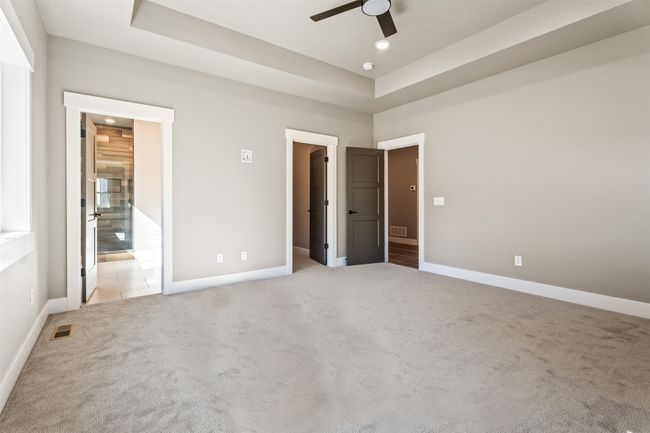 Unfurnished bedroom featuring light carpet, a walk in closet, baseboards, recessed lighting, and a raised ceiling | Image 22