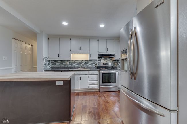 kitchen featuring tasteful backsplash, a sink, stainless steel appliances, under cabinet range hood, and wood finished floors | Image 12