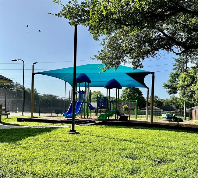 This photo shows a charming playground with slides and climbing structures under a blue canopy, surrounded by lush green grass and shaded by trees. Ideal for families seeking a home in a kid-friendly neighborhood. | Image 19