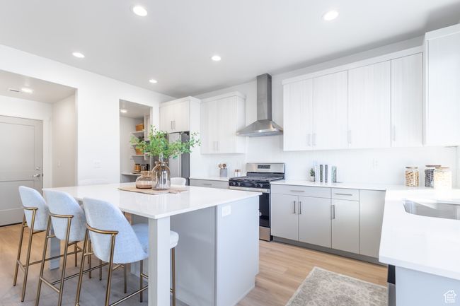 Kitchen with wall chimney range hood, appliances with stainless steel finishes, a kitchen island, a breakfast bar area, and light wood-type flooring | Image 9
