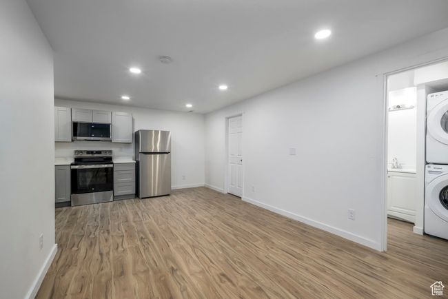 Basement kitchen featuring recessed lighting, stainless steel appliances, light wood finished floors, gray cabinetry, and stacked washer / drying machine | Image 26
