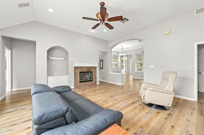 Living room with light wood finished floors, arched walkways, visible vents, and ceiling fan with notable chandelier | Image 7