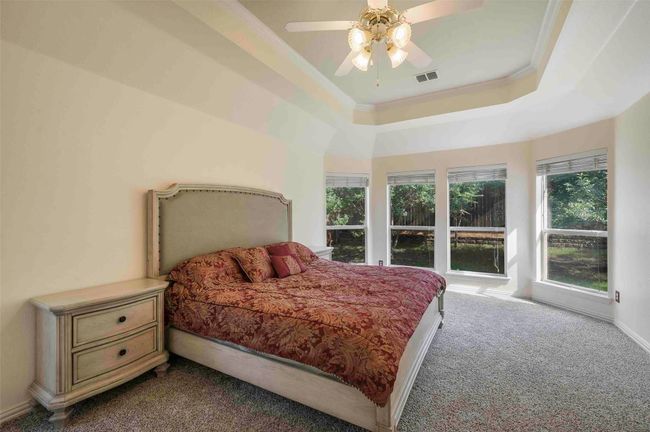 Bedroom with carpet flooring, visible vents, a ceiling fan, crown molding, and a tray ceiling | Image 6