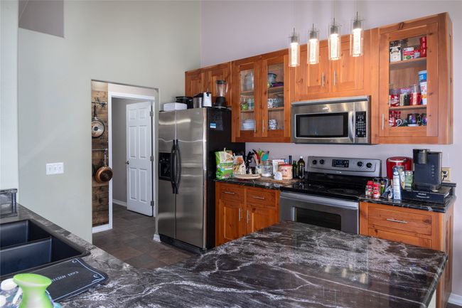 Kitchen featuring stainless steel appliances, glass insert cabinets, brown cabinetry, and dark stone countertops | Image 40