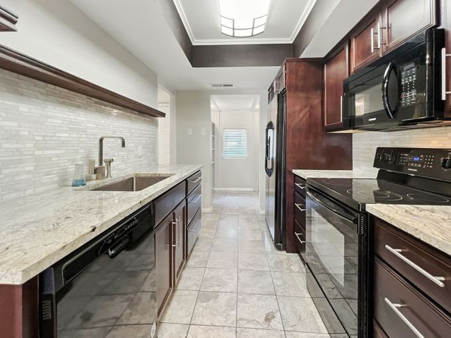 Kitchen with backsplash, black appliances, dark brown cabinets, crown molding, and light tile patterned floors | Image 4