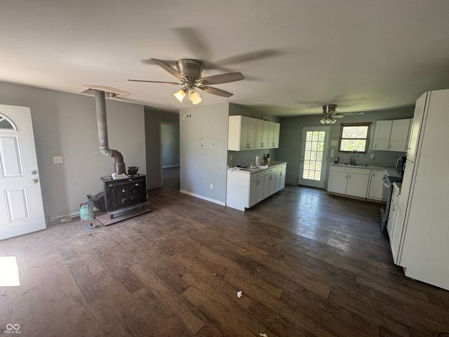 unfurnished living room featuring ceiling fan, a sink, baseboards, a wood stove, and dark wood-type flooring | Image 9