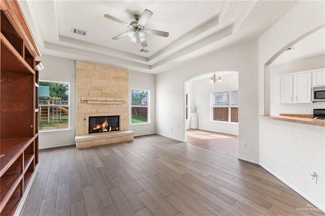 Unfurnished living room featuring a tray ceiling, arched walkways, healthy amount of natural light, and wood finished floors | Image 16