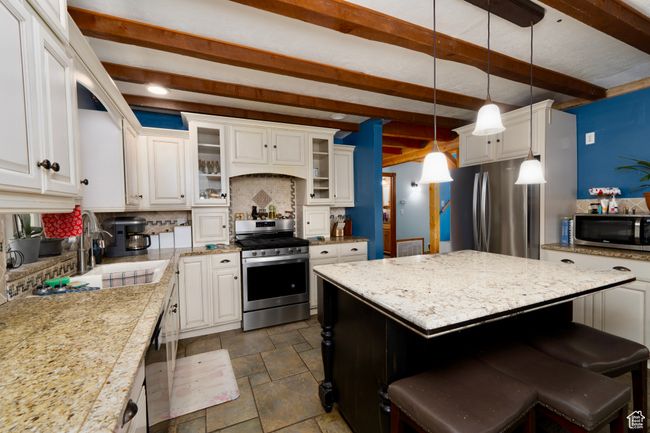 Kitchen featuring stainless steel appliances, stone tile flooring, decorative backsplash, a sink, and white cabinetry | Image 16