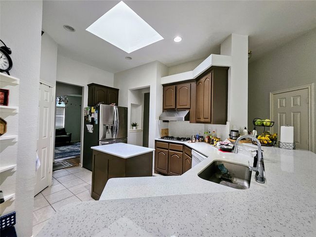 Kitchen featuring a skylight, under cabinet range hood, stainless steel fridge, dark brown cabinetry, and a center island | Image 7