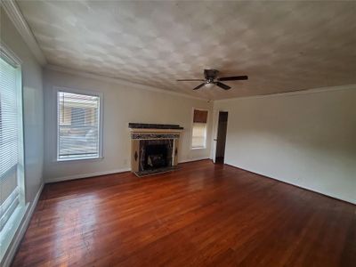 Unfurnished living room with dark wood-type flooring, a tile fireplace, ceiling fan, and crown molding | Image 3