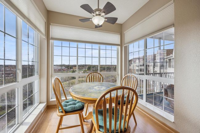 Bright, sun-filled breakfast nook is bathed in natural light from the 3 walls of windows, offering views of the pond and distant scenery from the 3rd floor. The space is accented with soft shades on the windows and a ceiling fan. | Image 12
