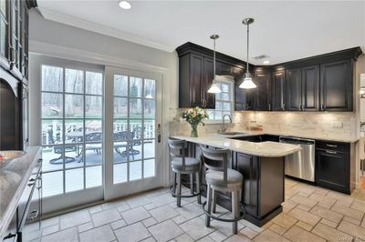 Kitchen featuring backsplash, light stone counters, sink, pendant lighting, and stainless steel dishwasher | Image 3