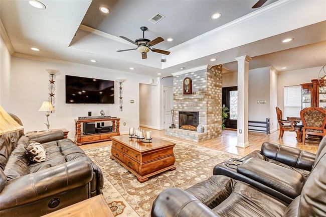 Spacious and inviting, the living area features high ceilings with twin ceiling fans for added comfort. A striking brick accent wall houses a fireplace, creating an attractive focal point. A large picture window frames a breathtaking view of the pool, while the open-concept design effortlessly connects the space to the kitchen and dining area. | Image 18