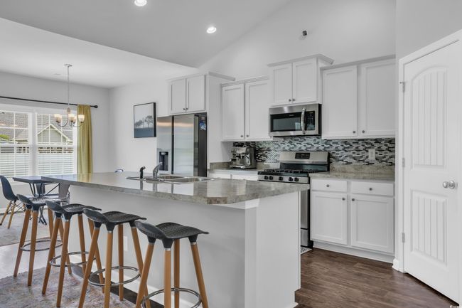 Kitchen with an island with sink, stainless steel appliances, backsplash, a breakfast bar area, and white cabinetry | Image 20