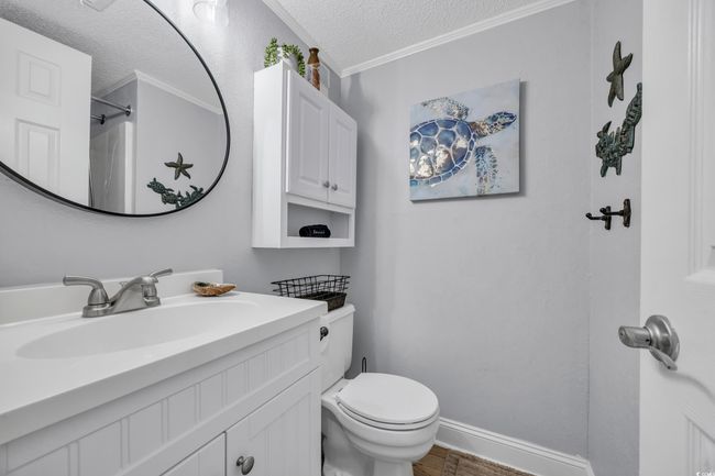 Bathroom featuring a textured ceiling, toilet, vanity, crown molding, and a shower | Image 11