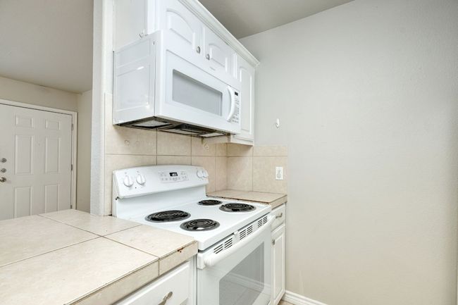 Kitchen featuring white appliances, tasteful backsplash, tile countertops, and white cabinets | Image 9