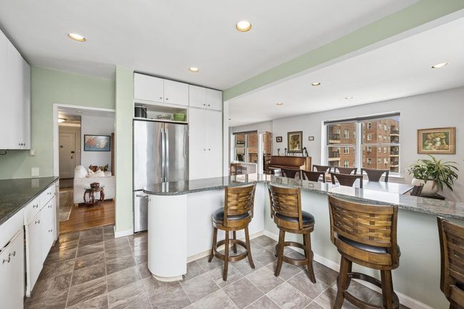 Kitchen featuring freestanding refrigerator, a breakfast bar, recessed lighting, white cabinetry, and dark stone counters | Image 5