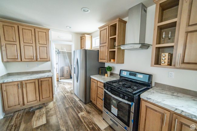 Kitchen with dark wood-style floors, open shelves, light stone countertops, wall chimney exhaust hood, and appliances with stainless steel finishes | Image 46