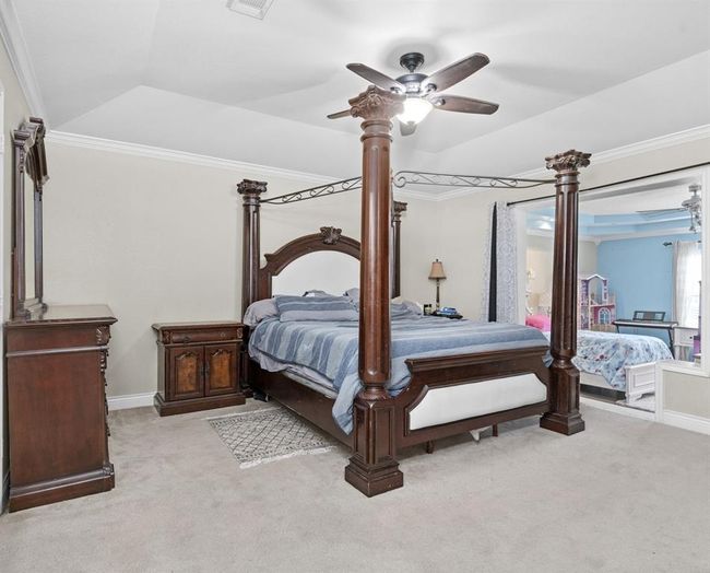 This is a spacious bedroom featuring a large four-poster bed, elegant wooden furniture, a ceiling fan with a light fixture, neutral carpeting, and a view into an adjoining room with blue walls. | Image 33