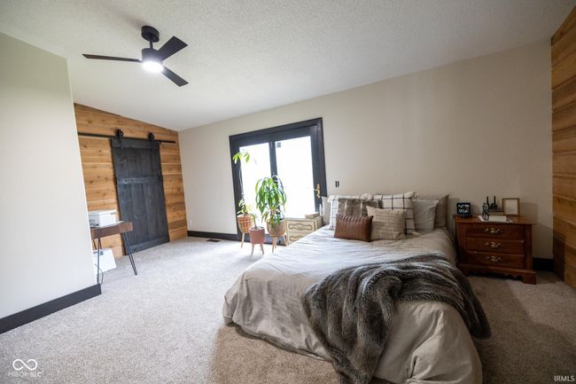 bedroom with wooden walls, a barn door, carpet, and vaulted ceiling | Image 9