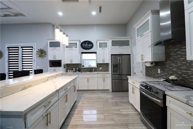 Kitchen featuring stainless steel fridge with ice dispenser, stove, wall chimney range hood, a sink, and backsplash | Image 5