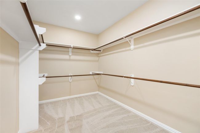 Ideal for organized living, this massive walk-in closet features ample hanging space, neutral walls, plush carpeting, and a high ceiling for an open, airy feel. | Image 24