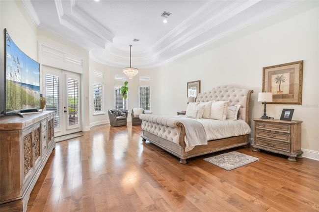 The expansive primary suite impresses with elegant tray ceilings, rich hardwood flooring, and a private sitting area bathed in natural light, creating a serene retreat. | Image 9