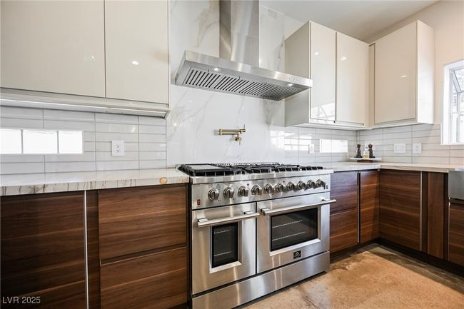 Kitchen with decorative backsplash, double oven range, wall chimney exhaust hood, and modern cabinets | Image 18